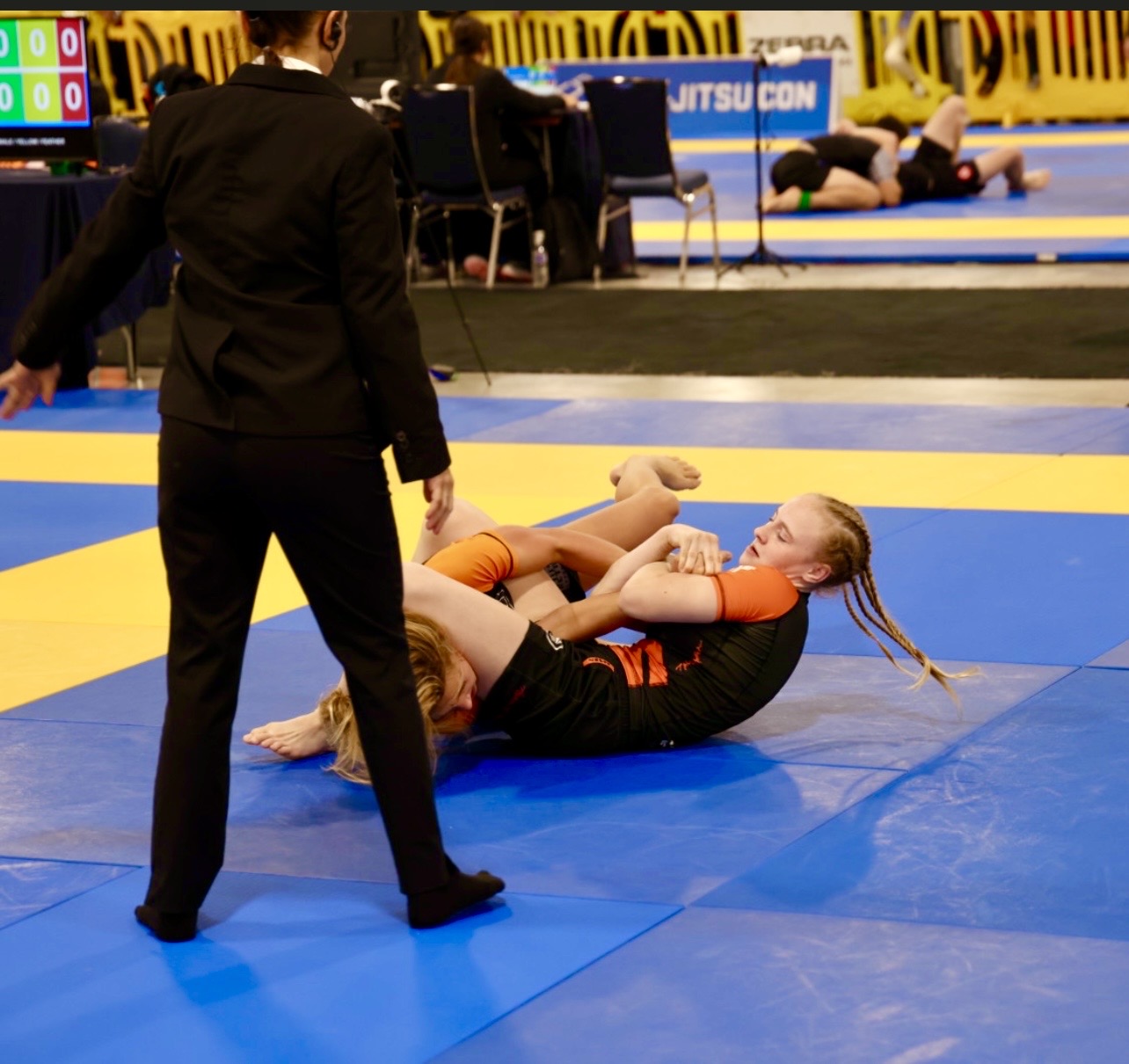 Competition image from the 2024 IBJJF Pan Kids No-Gi Championship bracket. The subject is shown in a top control position. IBJJF sanctioned competition environment with scoring table and adjacent mats visible in the background.
